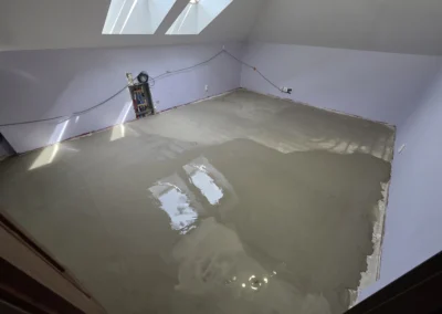 Zdjęcie przedstawia świeżo wylaną posadzkę samopoziomującą w rogu pokoju, gdzie widoczne są nierówności i mokre plamy.