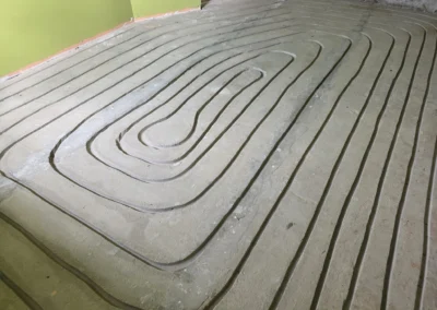 Bliskie ujęcie wyciętych, krętych rowków w szaro-zielonej płycie izolacyjnej, gotowej na rury ogrzewania podłogowego.