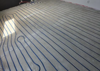 Widok z góry na niebieskie rury ogrzewania podłogowego, ułożone w jastrychu na podłożu cementowym.