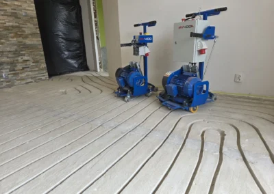 Wnętrze w trakcie prac budowlanych, na podłodze frezowane rowki pod rury ogrzewania, w tle dwie maszyny do frezowania.